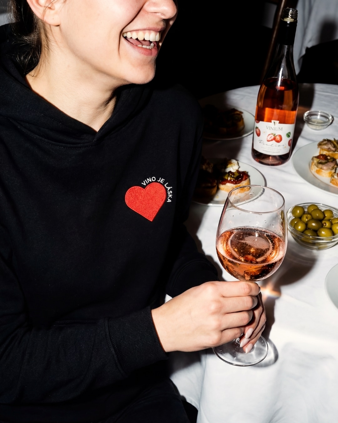 Žena pije perlivé víno z vinařství VINIUM Velké Pavlovice a má na sobě mikinu s výšivkou Víno je láska.